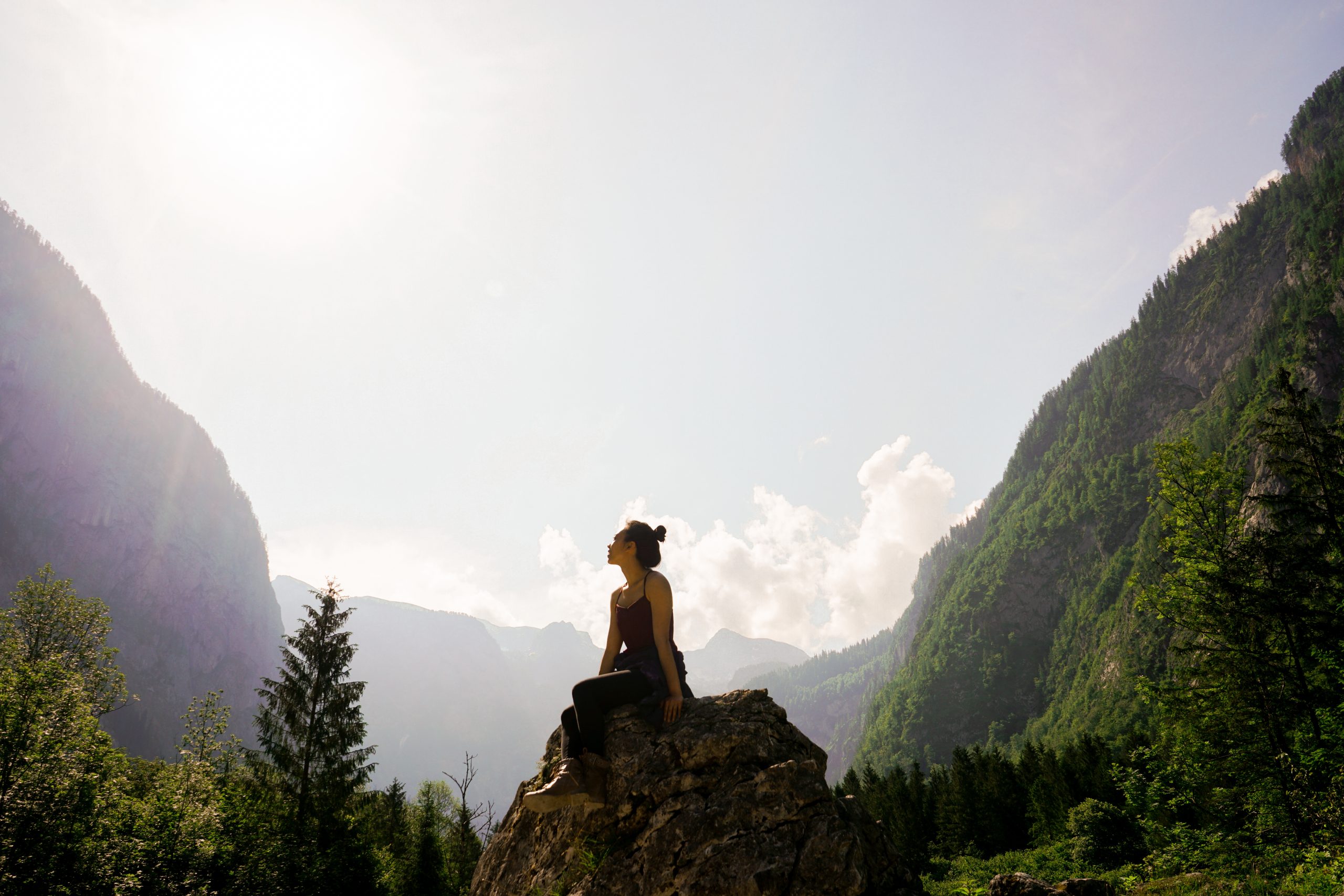 Une femme regardant vers le ciel assise sur un rocher au milieu de montagnes très vertes
